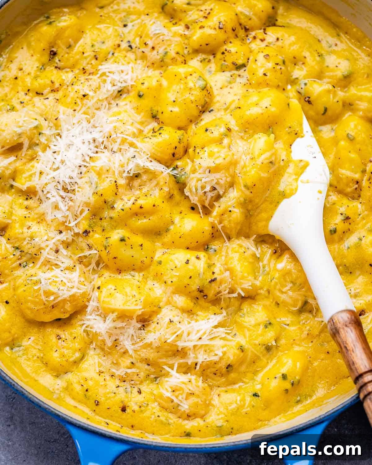 A closeup image of creamy pumpkin gnocchi in a blue skillet, garnished with fresh sage leaves and grated Parmesan cheese.