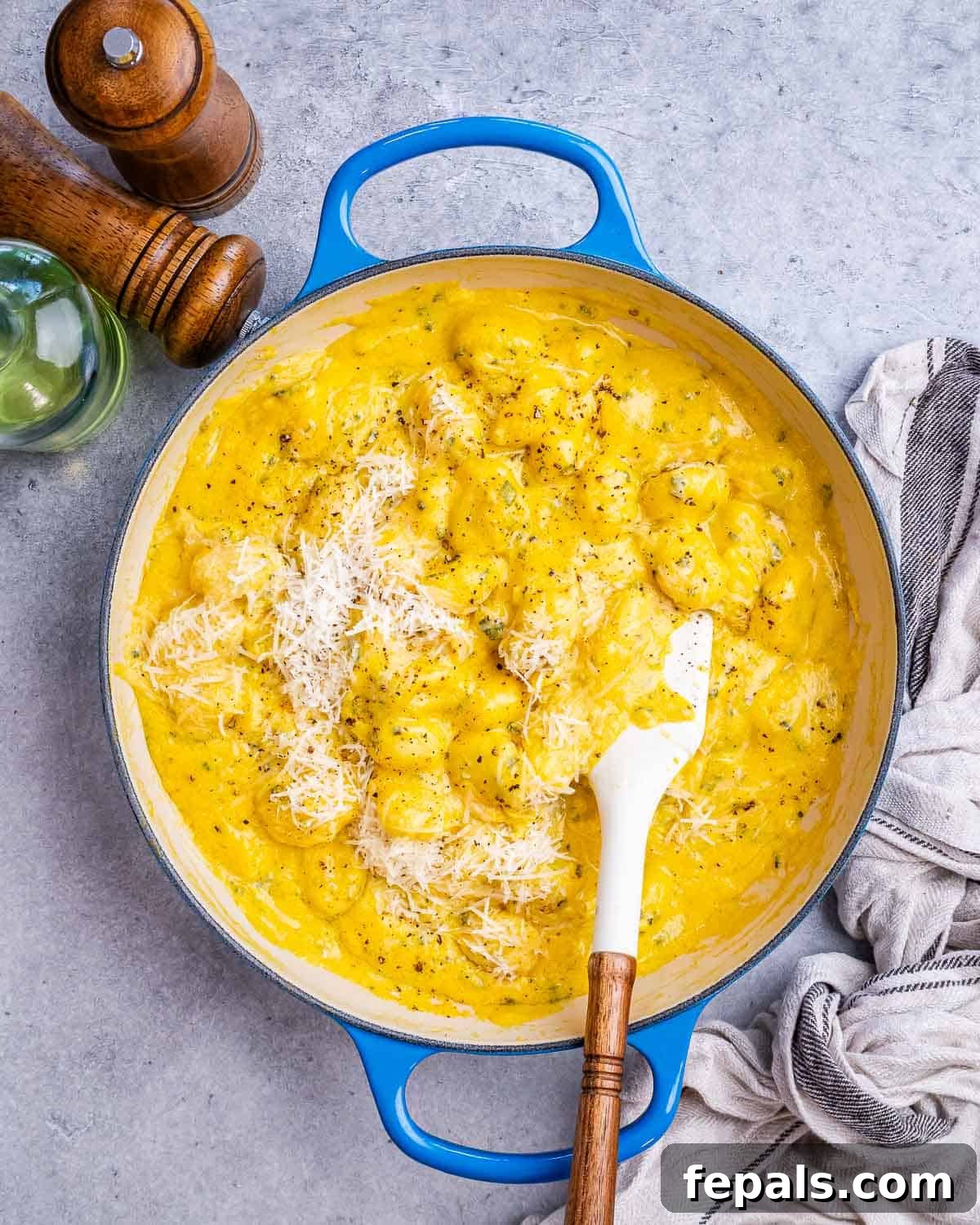 A blue skillet filled with creamy pumpkin gnocchi, served with a white spatula and fresh sage garnish.