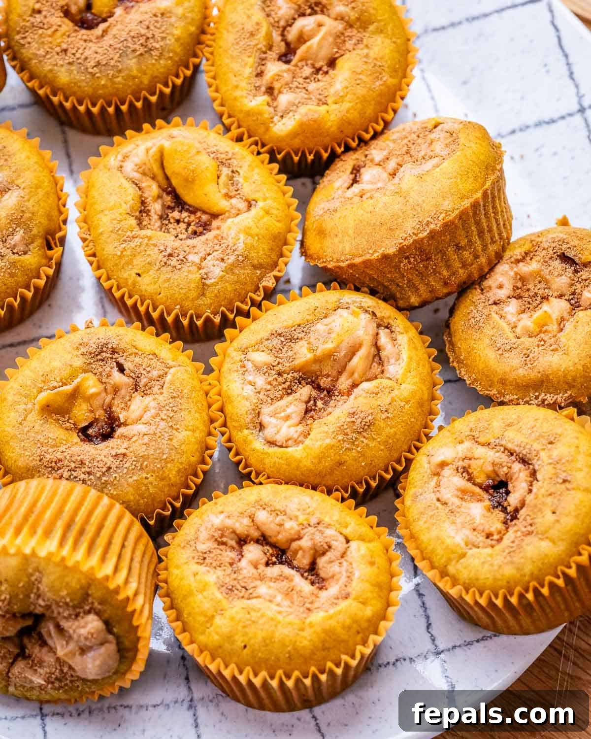 Spiced Pumpkin Cream Cheese Swirl Muffins 2 A plate featuring several golden-brown pumpkin muffins, generously stuffed with a visible cream cheese filling, and a delicate dusting of cinnamon sugar.
