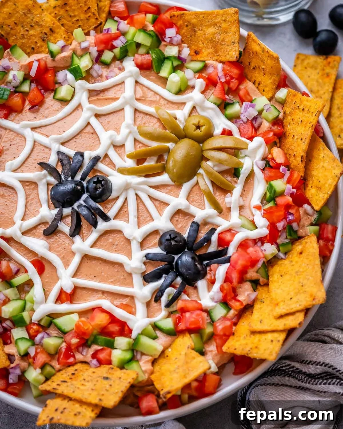 Close-up of the spider web design made with sour cream over the taco dip, with veggies around the edges.