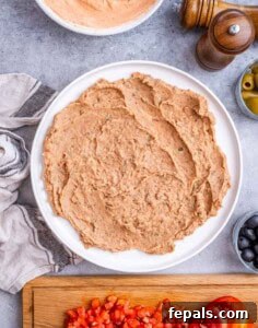 Layer of refried beans spread evenly in a round white serving dish as the base of the dip.