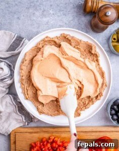 Cream cheese and Greek yogurt mixture spread over the beans in the serving dish with a white spatula.