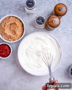 Whisk mixing the Greek yogurt, cream cheese, and seasoning together in a glass bowl.