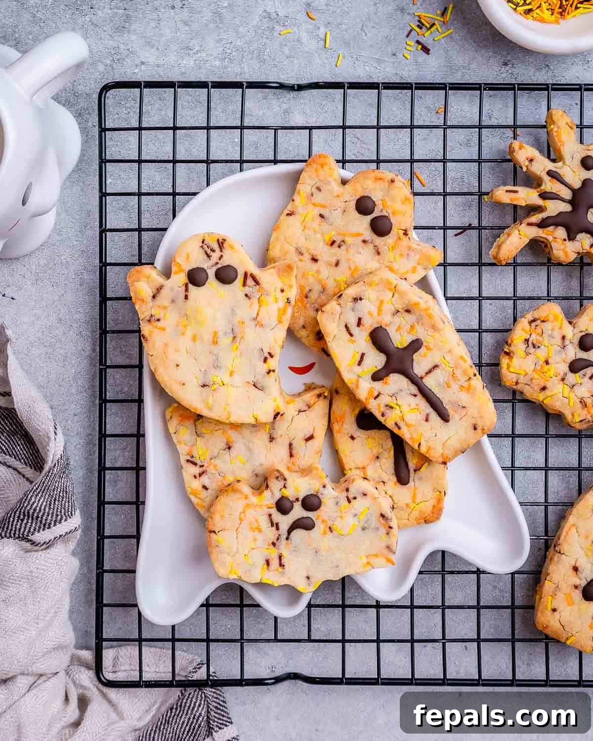 Spooktacularly Easy Halloween Cookies Kids Will Love 2 Assortment of Halloween-shaped sugar cookies on a plate, featuring ghost and spider designs, with a cooling rack in the background.