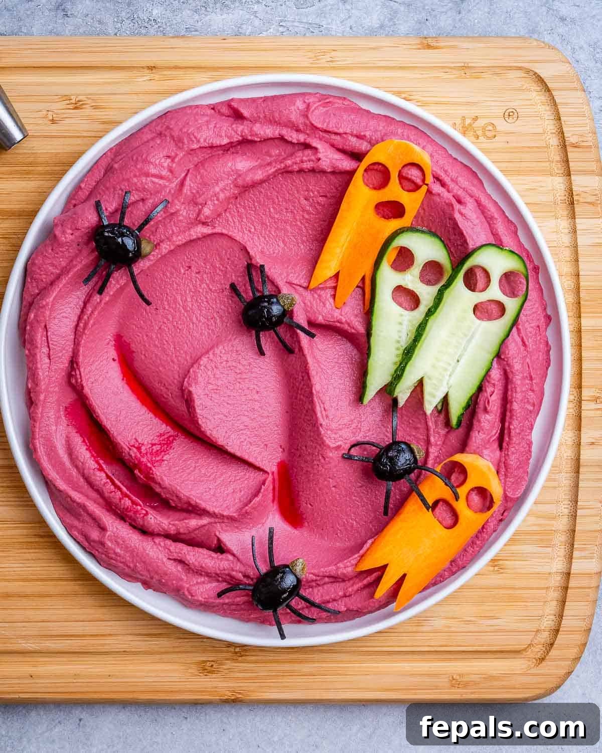 red looking hummus in a bowl topped with spider-looking olives.