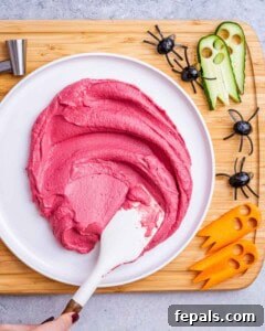 spreading beet hummus over a plate with a spatula.