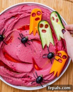 hand adding ghost veggies over beet hummus.