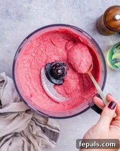 hand holding spoon and spooning some hummus from blender.