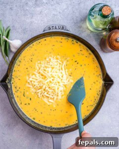 Shredded cheddar cheese melting into the pumpkin sauce in a skillet, creating a creamy texture.