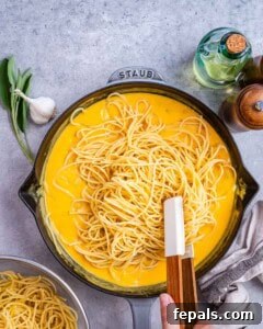 Cooked pasta being added to and tossed with the creamy pumpkin Alfredo sauce in a skillet.