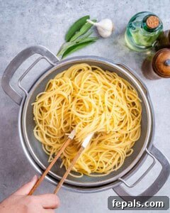Cooked pasta in a pot, ready to be drained, with a measuring cup to reserve pasta water.