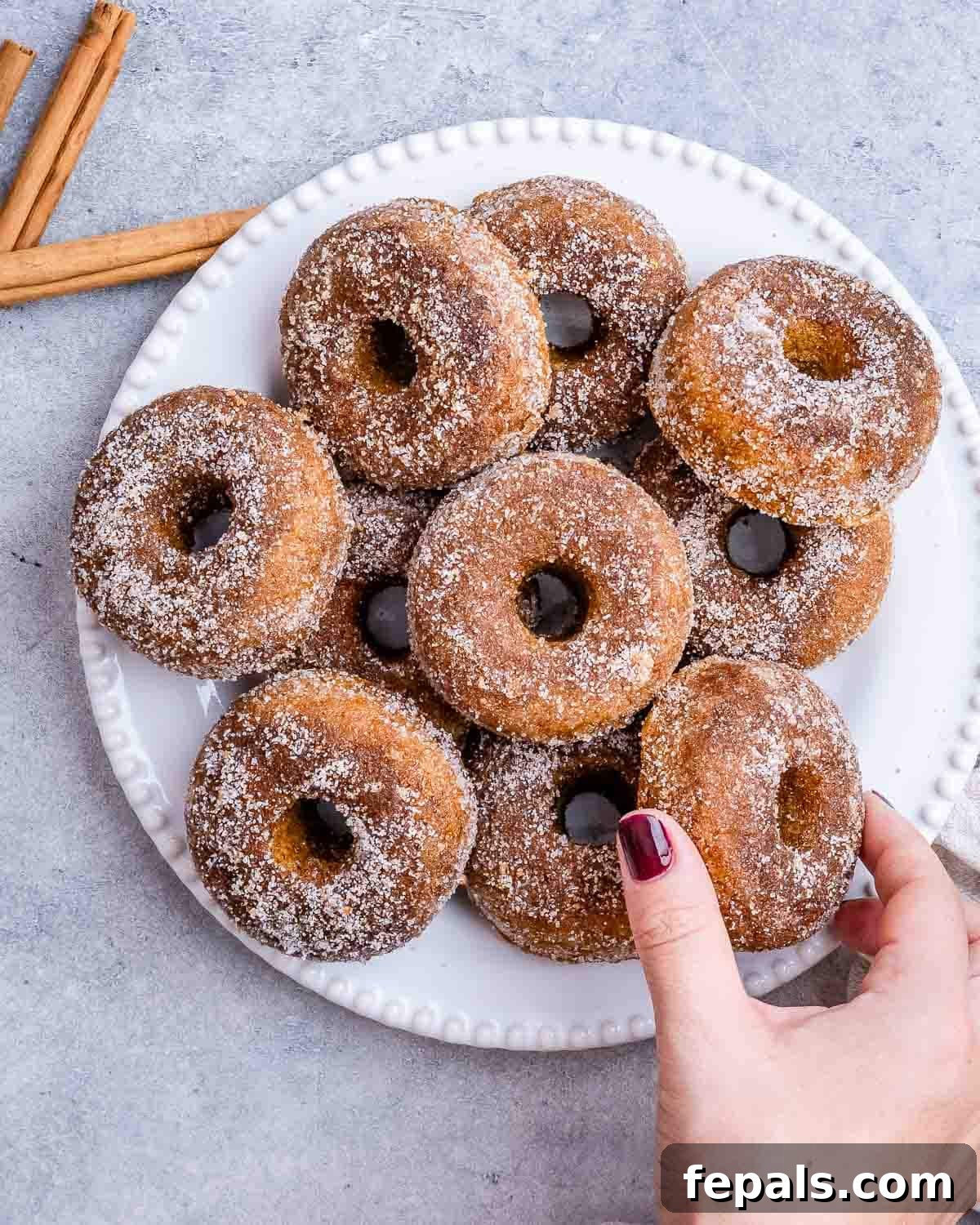 A hand reaching for a delicious baked pumpkin donut from a plate.