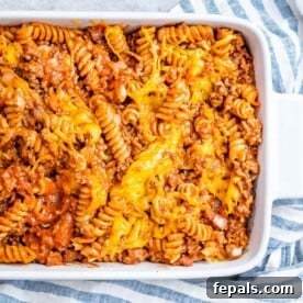 A hearty casserole in a pristine white dish, showcasing perfectly cooked rotini pasta nestled in a rich, meaty tomato sauce, generously topped with golden-brown melted cheese.