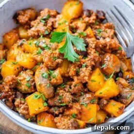 A hearty bowl of Cowboy Casserole, showcasing seasoned ground beef, tender potatoes, and vibrant vegetables cooked in a rich, flavorful red sauce.