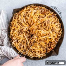 A hand holding tongs, expertly stirring a skillet filled with glossy, flavorful Mongolian ground beef and tender noodles, ready to be served.
