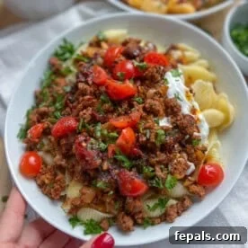 Perfectly cooked pasta topped with a generous serving of seasoned beef and garnished with vibrant chopped tomatoes and fresh parsley in an elegant dish.