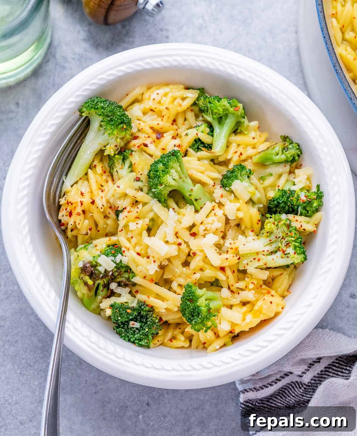 A white bowl filled with creamy broccoli cheddar orzo, garnished with fresh parsley.