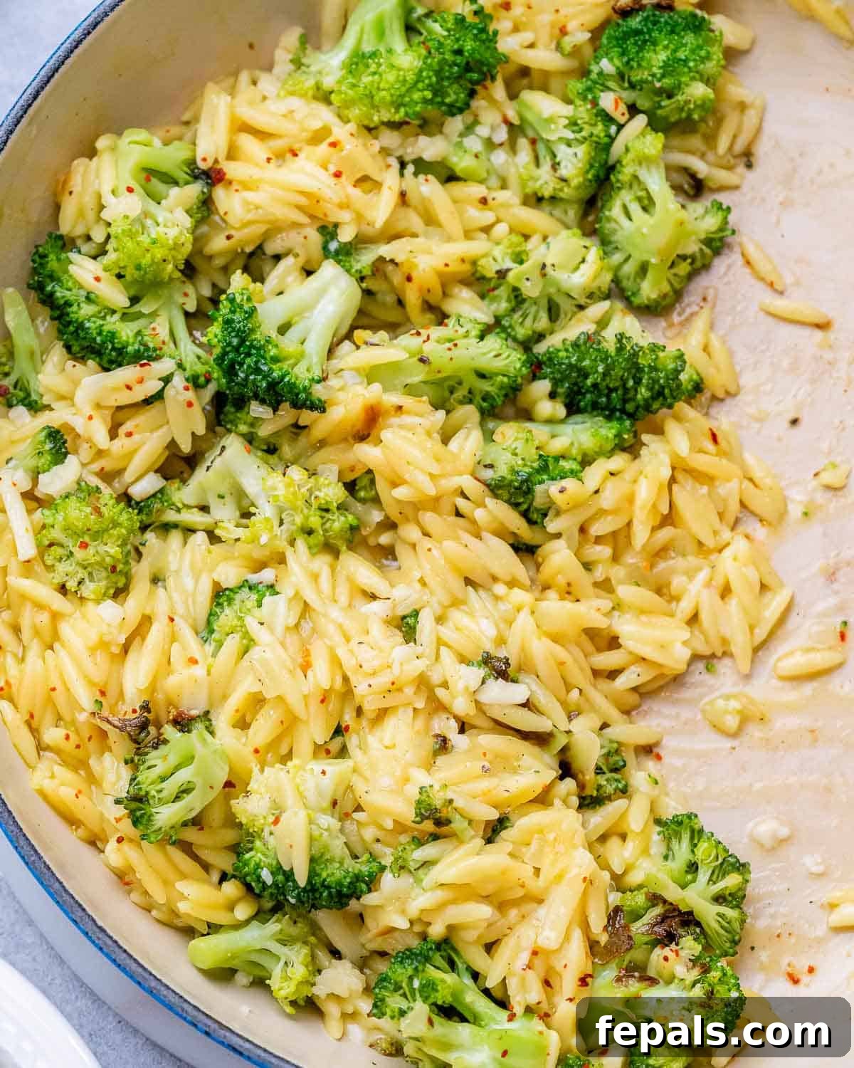 A close-up view of a pan full of creamy broccoli cheddar orzo, ready to be served.