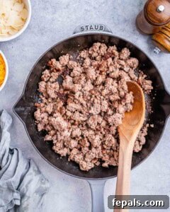 Savory Butternut Squash & Beef Ragu Pasta 11 Ground beef browning in a skillet with a wooden spoon stirring.