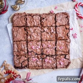 Brownies cut into perfect squares, artfully arranged on parchment paper and topped with a scattering of vibrant chopped peppermint pieces, ready to be enjoyed.