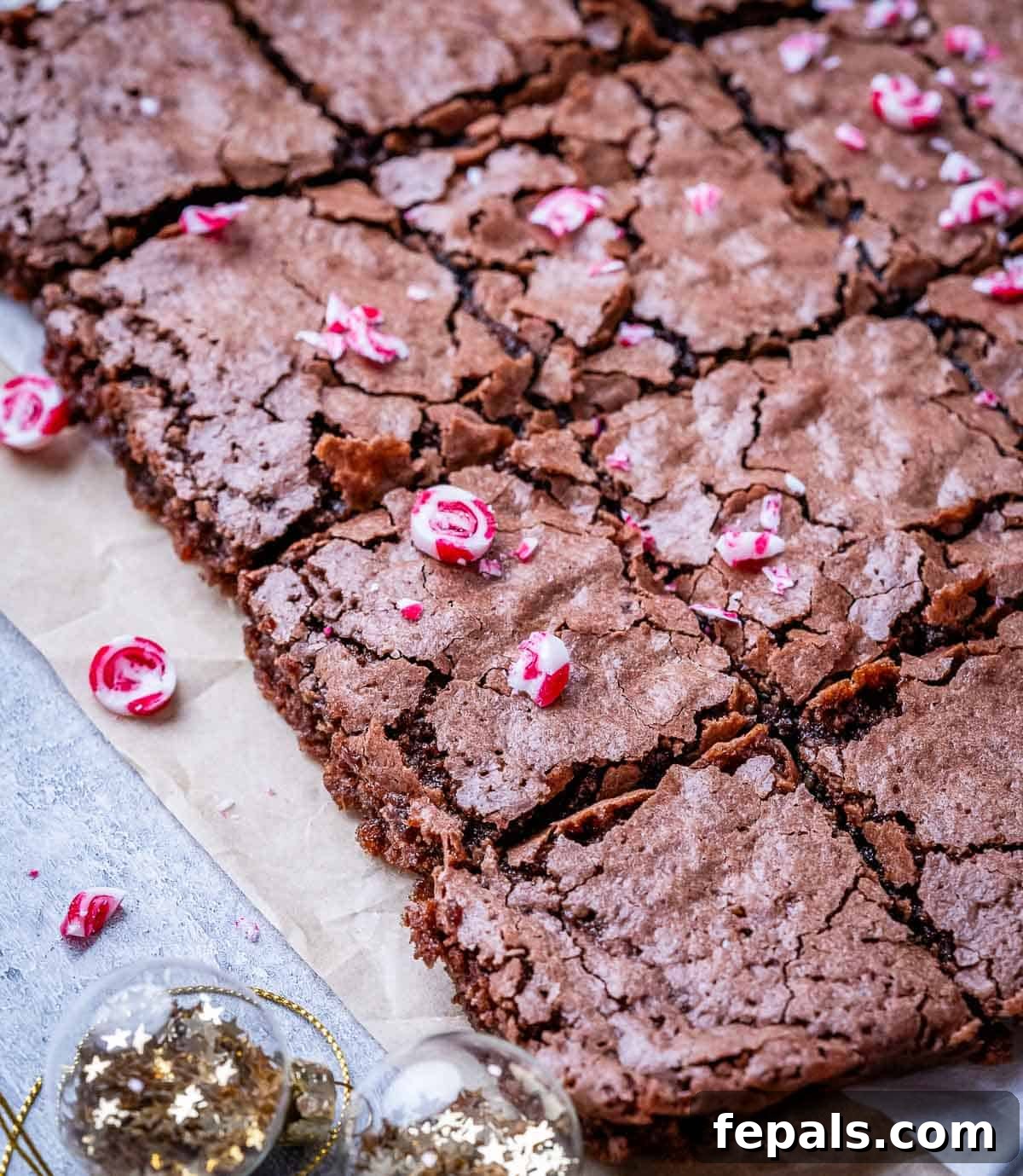 Cool Mint Fudge Brownies 7 A close-up view of freshly baked peppermint brownies, showcasing their beautiful crackly tops and vibrant red and white crushed candy canes scattered across each square.