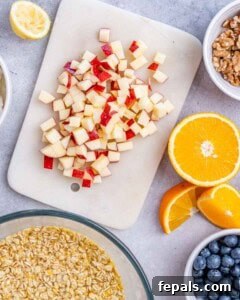 Chopped apple on a cutting board, next to a bowl with overnight oats soaking in orange juice.