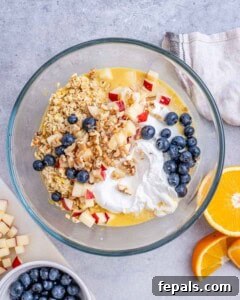 All overnight oat ingredients, including yogurt and blueberries, added to a bowl and ready to be mixed.