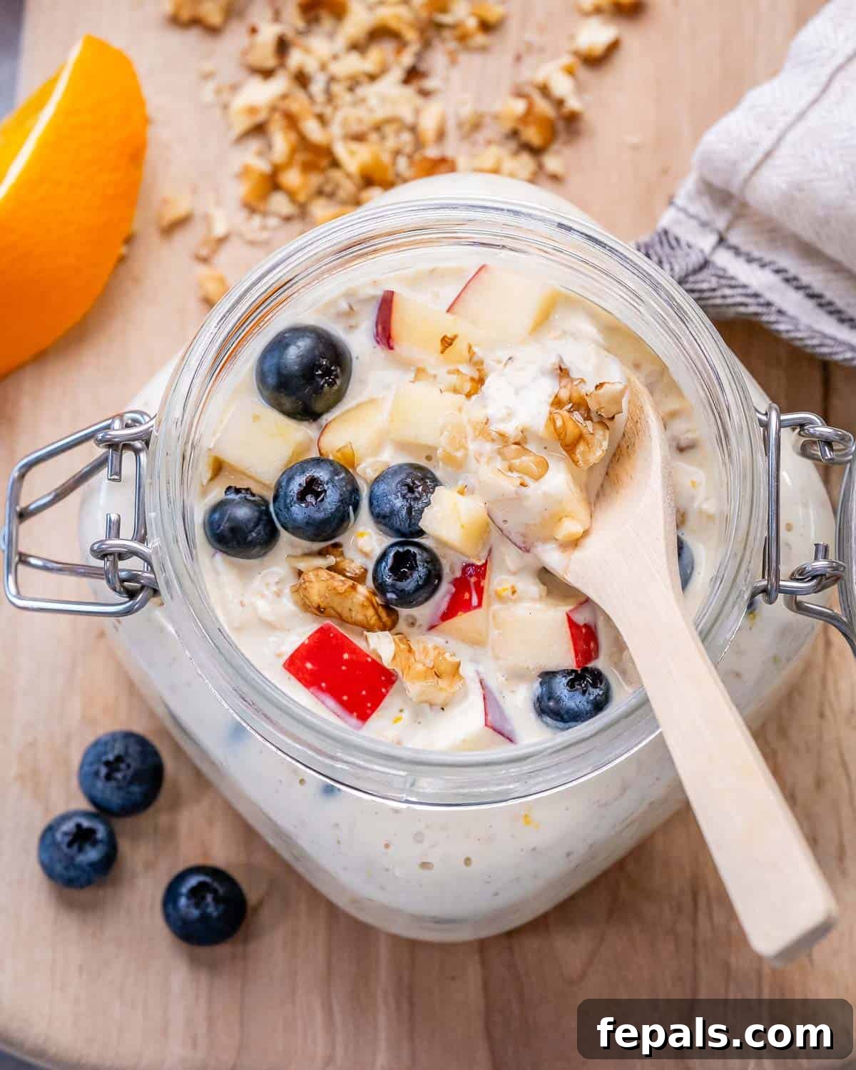 A spoon in a jar with Princess Diana's overnight oats, topped with fresh blueberries and chopped apples, ready to be enjoyed.