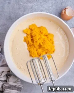 Decadent Pumpkin Spice Cheesecake Bars 11 Creamy cheesecake mixture in a bowl with pumpkin puree added on top, ready to be mixed together.