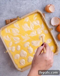 Decadent Pumpkin Spice Cheesecake Bars 12 Baking dish lined with crust, as pumpkin and plain cheesecake batters are being swirled together before baking.