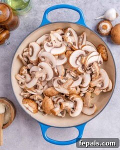 Mushrooms cooking in olive oil in a blue skillet over medium heat.