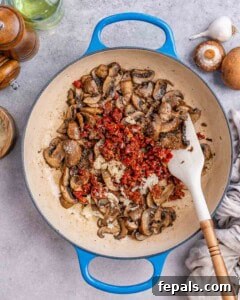Mushrooms sautéing with chopped sun-dried tomatoes and garlic in the skillet.