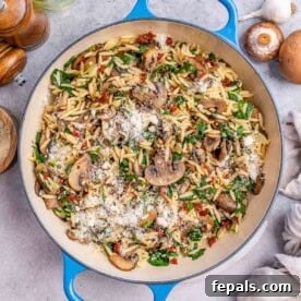 Overhead view of Mushroom Spinach Orzo sprinkled with parmesan cheese in a skillet.