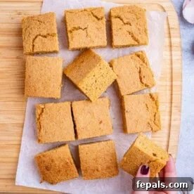 Freshly baked sweet potato cornbread cut into neat golden squares on parchment paper, with a hand holding a piece of sweet potato cornbread.