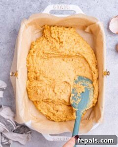 Golden Gluten Free Sweet Potato Cornbread 15 The cornbread batter being spread evenly into a parchment-lined baking dish with a spatula.