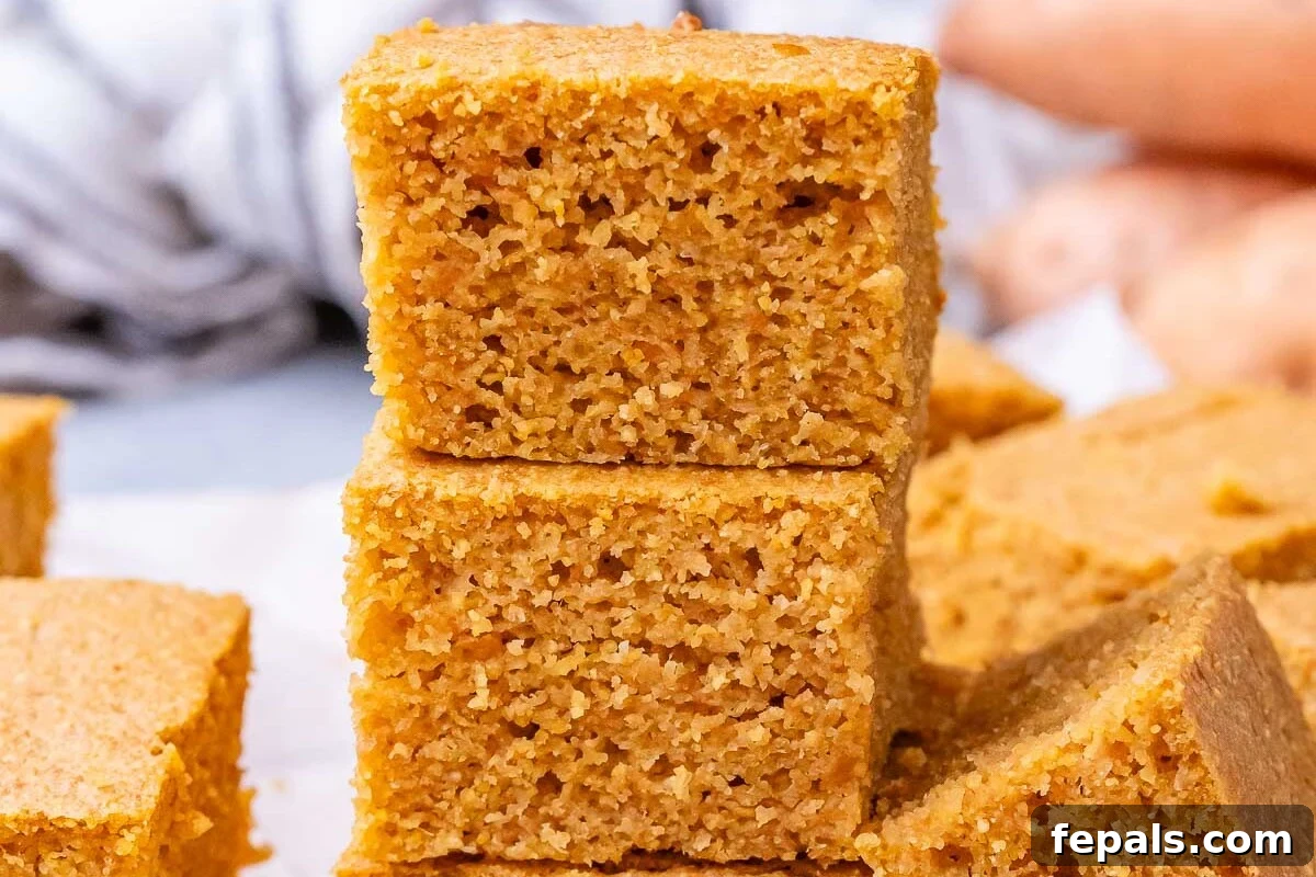 Golden Gluten Free Sweet Potato Cornbread 7 A stack of thick, golden sweet potato cornbread pieces balanced on a cutting board.
