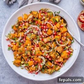 Mixed sweet potato salad in a white bowl with spoon, showing even coating of dressing and fresh herbs throughout.
