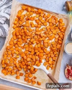 Roasted sweet potato cubes spread evenly on a parchment-lined baking sheet, golden and caramelized after baking.