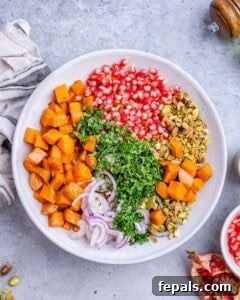 Ingredients for sweet potato salad arranged in a bowl: roasted potatoes, chopped parsley, red onion, pomegranate seeds, and pistachios.