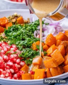 Pouring homemade dressing over roasted sweet potatoes and sliced onions in a large mixing bowl.