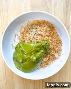 Toasted Kataifi in a bowl with pistachio cream and tahini, being mixed to combine.
