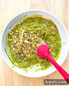 Crushed pistachios being added to the pistachio Kataifi mixture in a bowl.