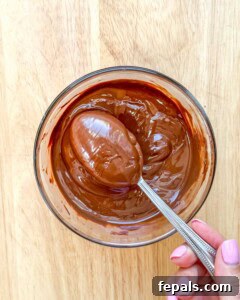 A spoon stirring melted chocolate and coconut oil in a bowl until smooth.