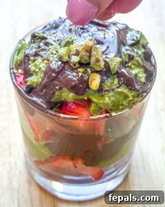 A Dubai strawberry cup being garnished with chopped pistachios on top of the chocolate layer.