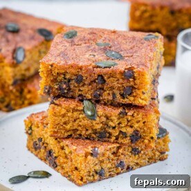 Three perfectly stacked pumpkin cake squares on a plate, showcasing their moist texture and inviting fall color, ready to be enjoyed.