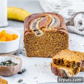 A beautifully baked loaf of pumpkin banana bread resting on a flat surface, with two inviting slices already cut and ready to serve.