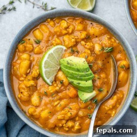 Top view of a generously sized bowl of rich orange pumpkin chili, topped with a sprinkle of pumpkin seeds and a spoon resting inside, accompanied by a side of crispy crackers.
