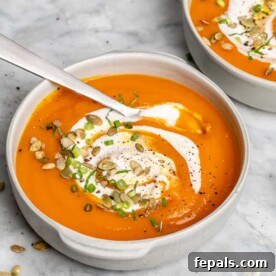 A steaming bowl of rich, orange roasted pumpkin soup, elegantly garnished with a swirl of cream and fresh herbs, ready to be savored as a comforting fall meal.