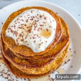 Top view of fluffy pumpkin pancakes topped with creamy yogurt, a drizzle of maple syrup, and a sprinkle of cinnamon, ready for a cozy fall breakfast.