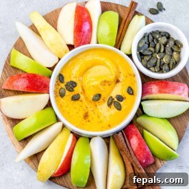 A pristine white bowl filled with a creamy pumpkin pie fruit dip, surrounded by perfectly sliced apples, ready for a delicious fall snack or appetizer.